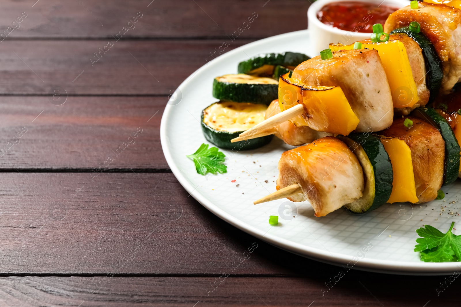 Photo of Delicious chicken shish kebabs with vegetables on wooden table, closeup. Space for text