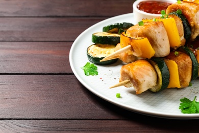 Photo of Delicious chicken shish kebabs with vegetables on wooden table, closeup. Space for text
