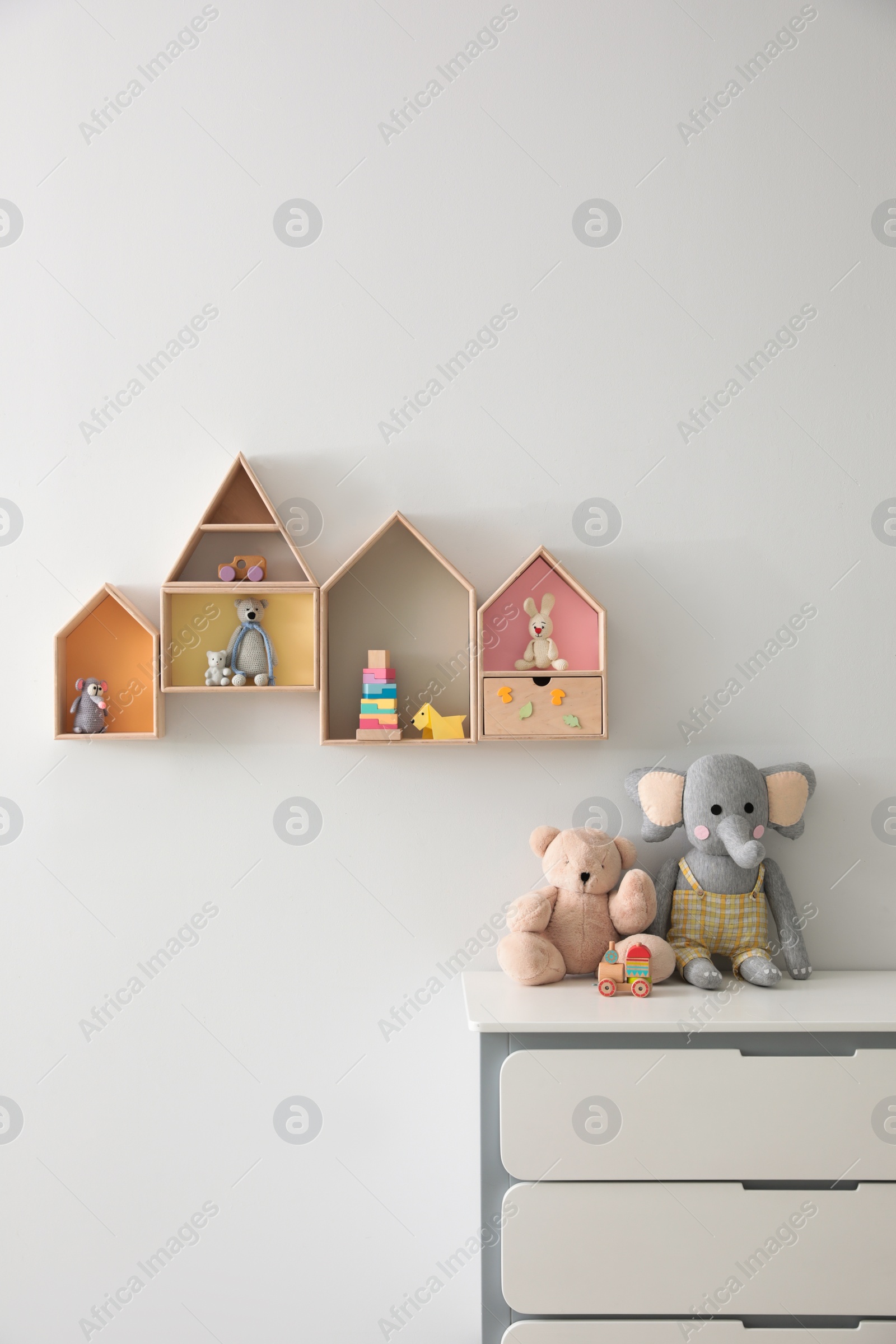 Photo of House shaped shelves and chest of drawers with toys in children's room. Interior design