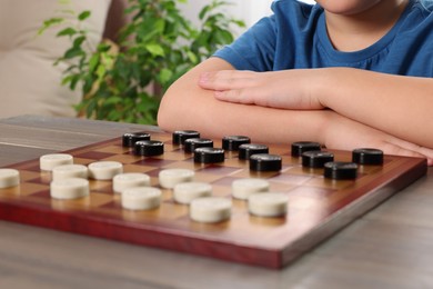 Photo of Playing checkers. Boy thinking about next move at table in room, closeup