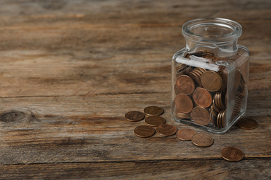 Glass jar with coins on wooden table, space for text