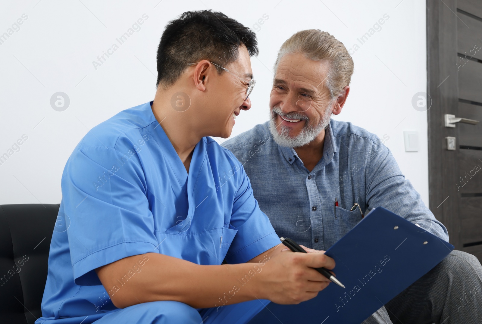 Photo of Doctor with clipboard consulting senior patient in clinic