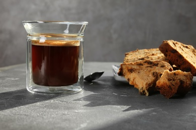 Glass of delicious coffee and plate with cake on grey table