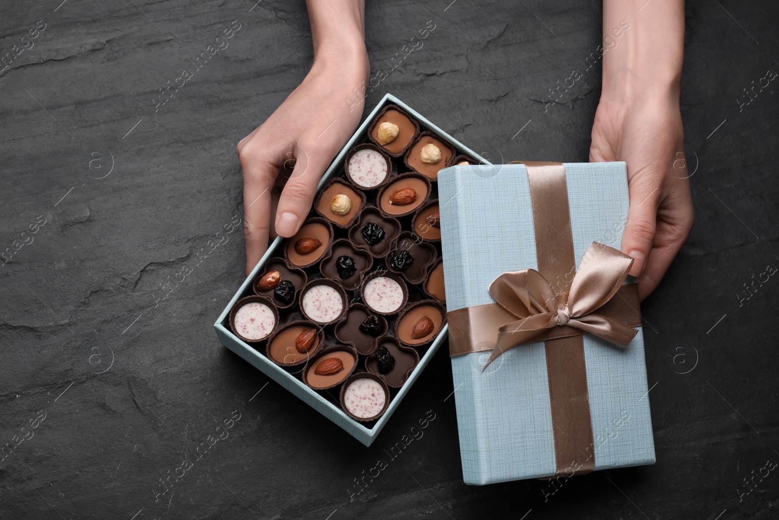 Photo of Woman with open box of delicious chocolate candies at black table, top view