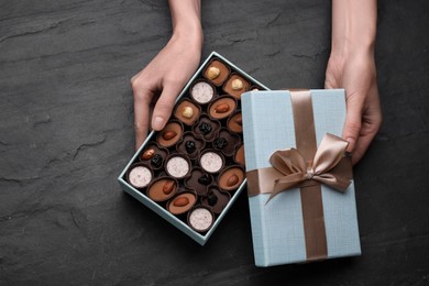 Woman with open box of delicious chocolate candies at black table, top view