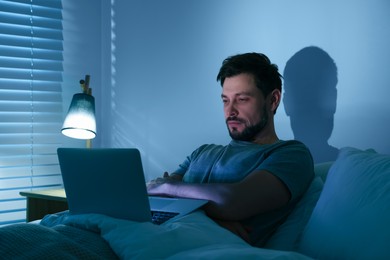 Photo of Man using laptop in bed at night. Internet addiction