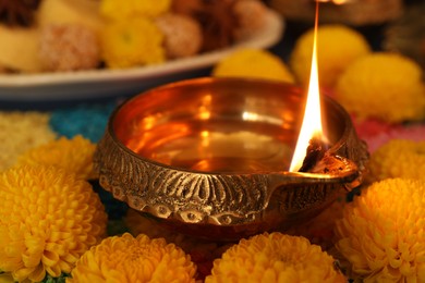 Diwali celebration. Diya lamp and chrysanthemum flowers on table, closeup