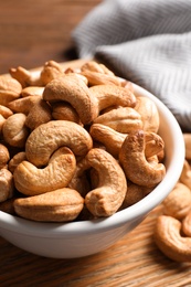 Photo of Tasty cashew nuts in bowl on table, closeup