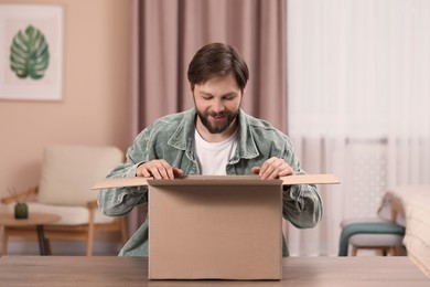 Photo of Happy man opening parcel at home. Internet shopping