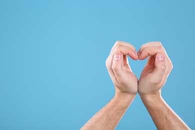 Man making heart with his hands on color background, space for text