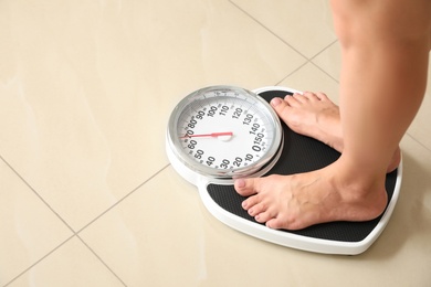 Woman standing on scales indoors, space for text. Overweight problem