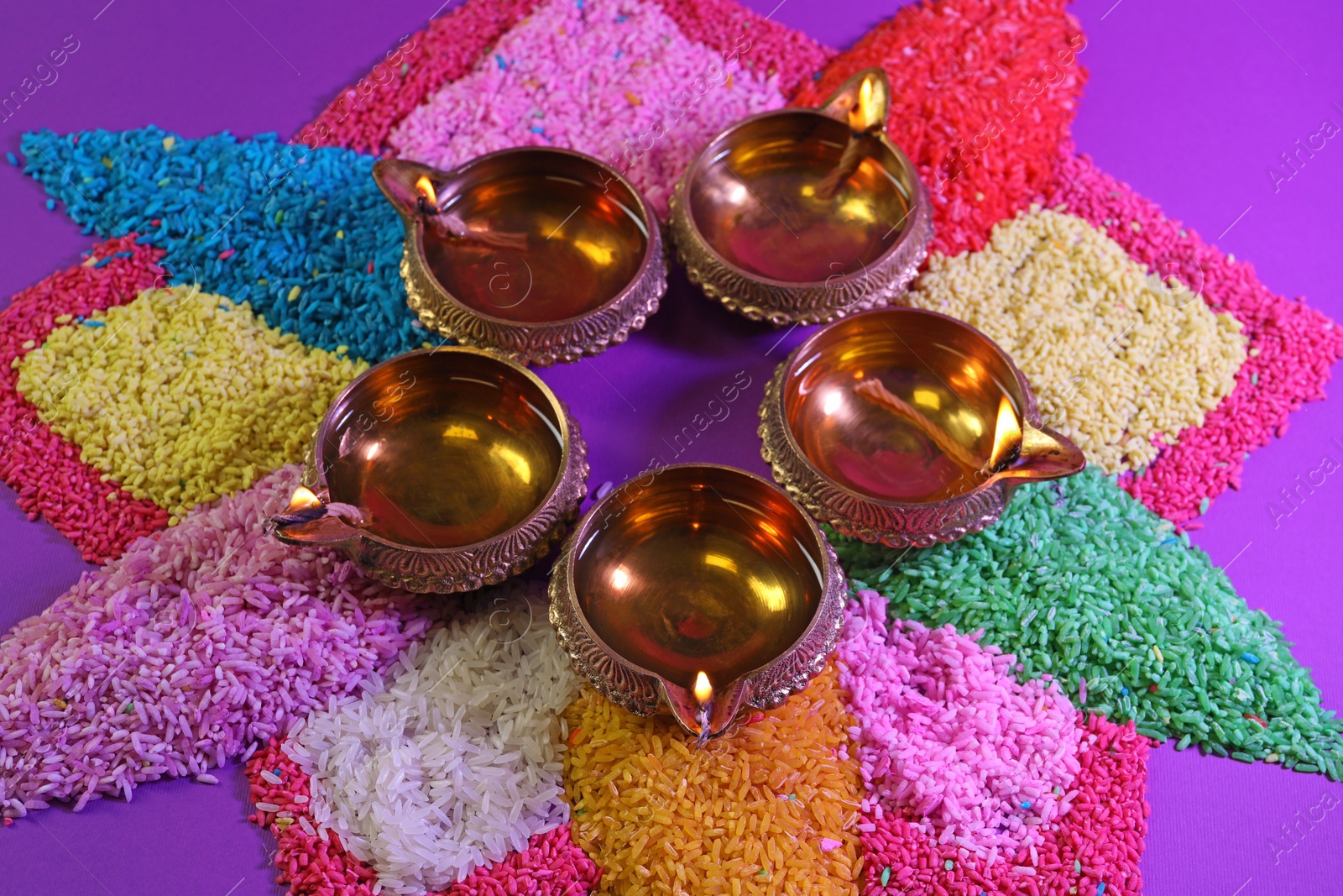 Photo of Diwali celebration. Diya lamps and colorful rangoli on purple background