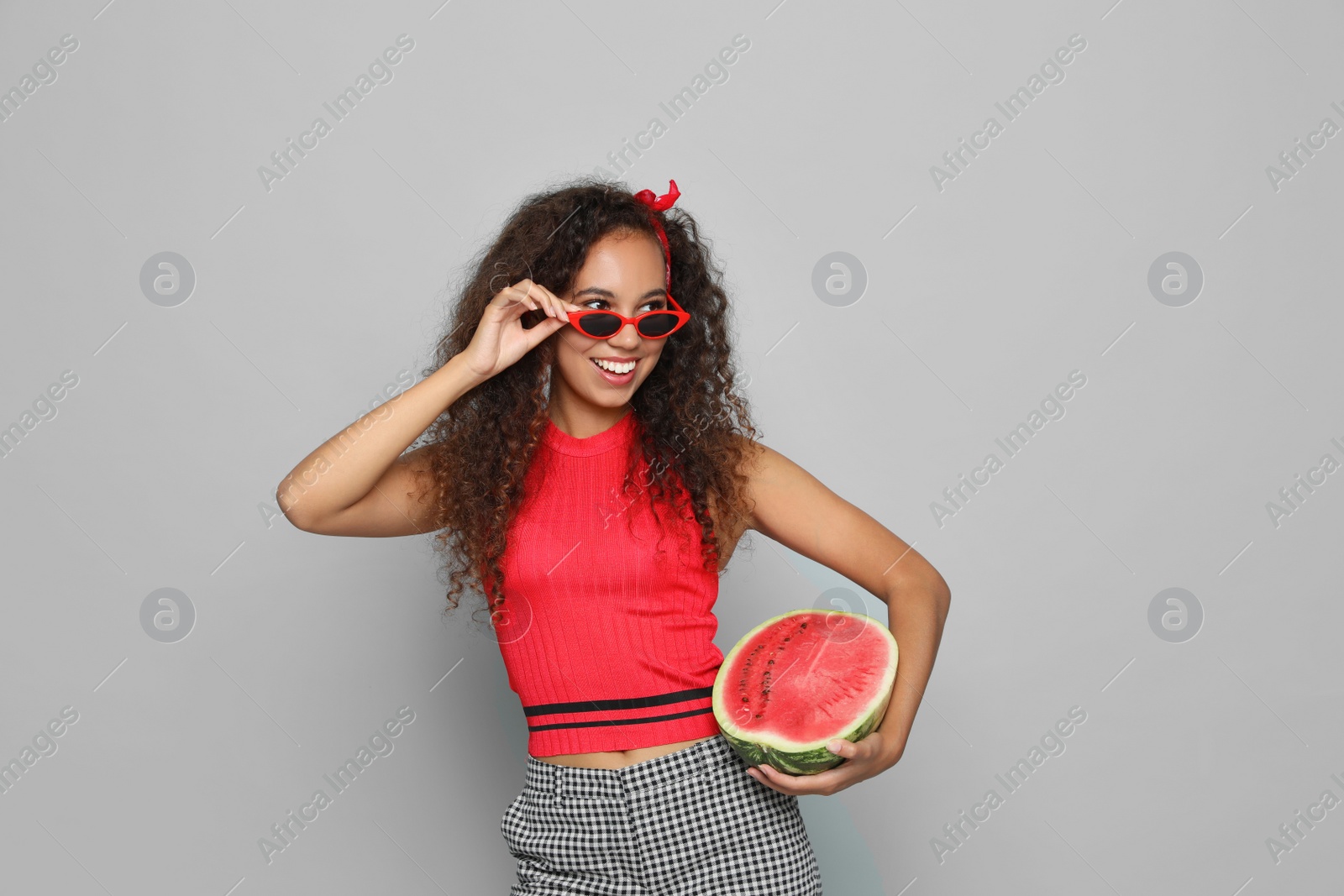 Photo of Beautiful young African American woman with half of watermelon on grey background