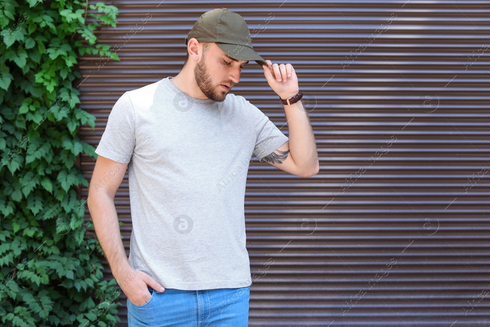 Photo of Young man wearing gray t-shirt near wall on street. Urban style