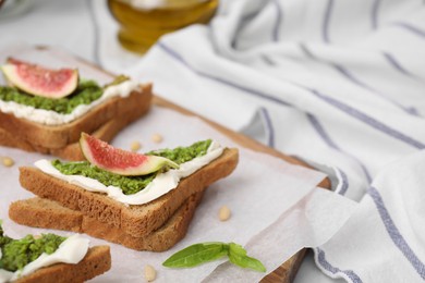 Photo of Tasty bruschetta with cream cheese, pesto sauce and fig on parchment paper, closeup