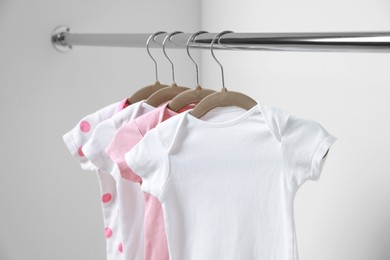 Baby bodysuits hanging on rack near white wall, closeup