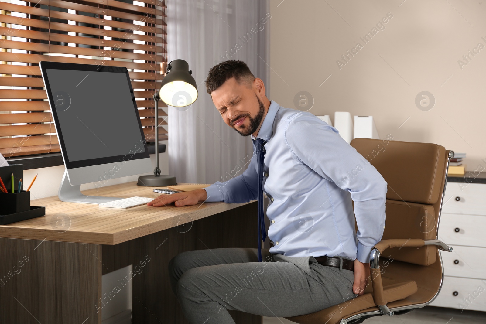 Photo of Man suffering from hemorrhoid at workplace in office