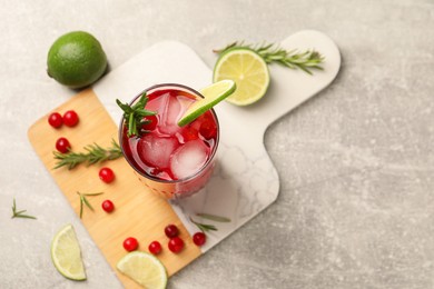 Photo of Tasty cranberry cocktail with rosemary and lime in glass on gray table, top view. Space for text