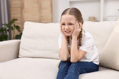 Photo of Little girl suffering from headache on sofa indoors. Space for text