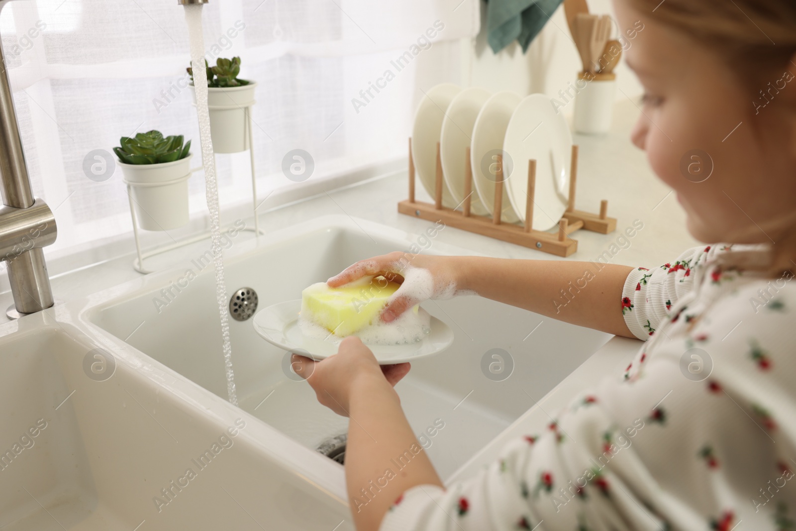 Photo of Little girl washing plate above sink indoors, closeup