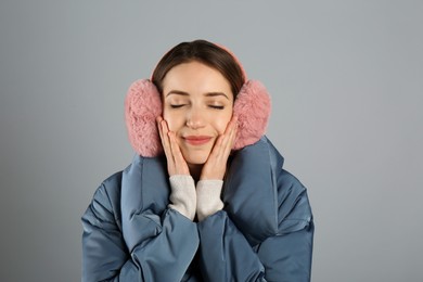 Photo of Happy woman wearing warm earmuffs on grey background