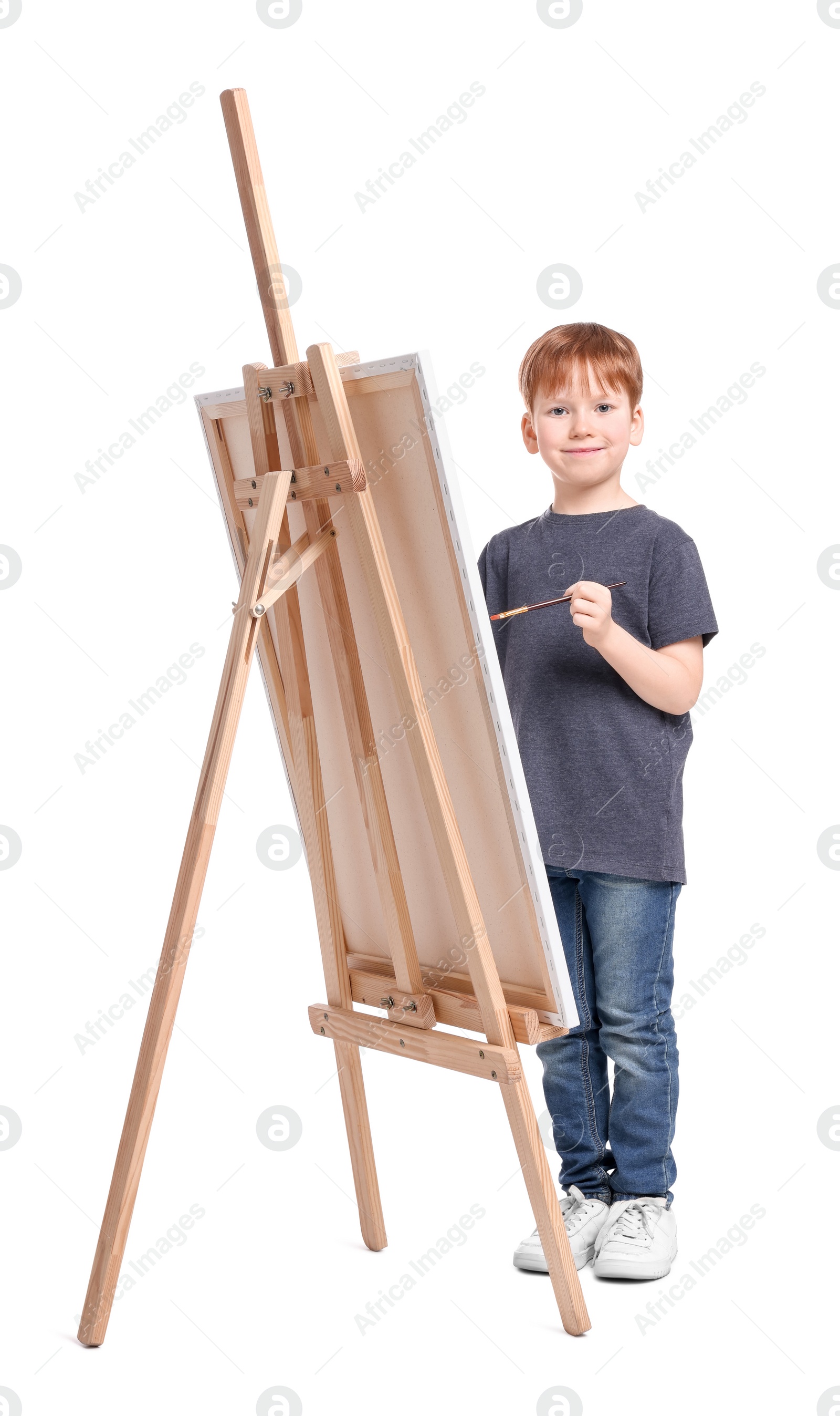 Photo of Little boy painting against white background. Using easel to hold canvas