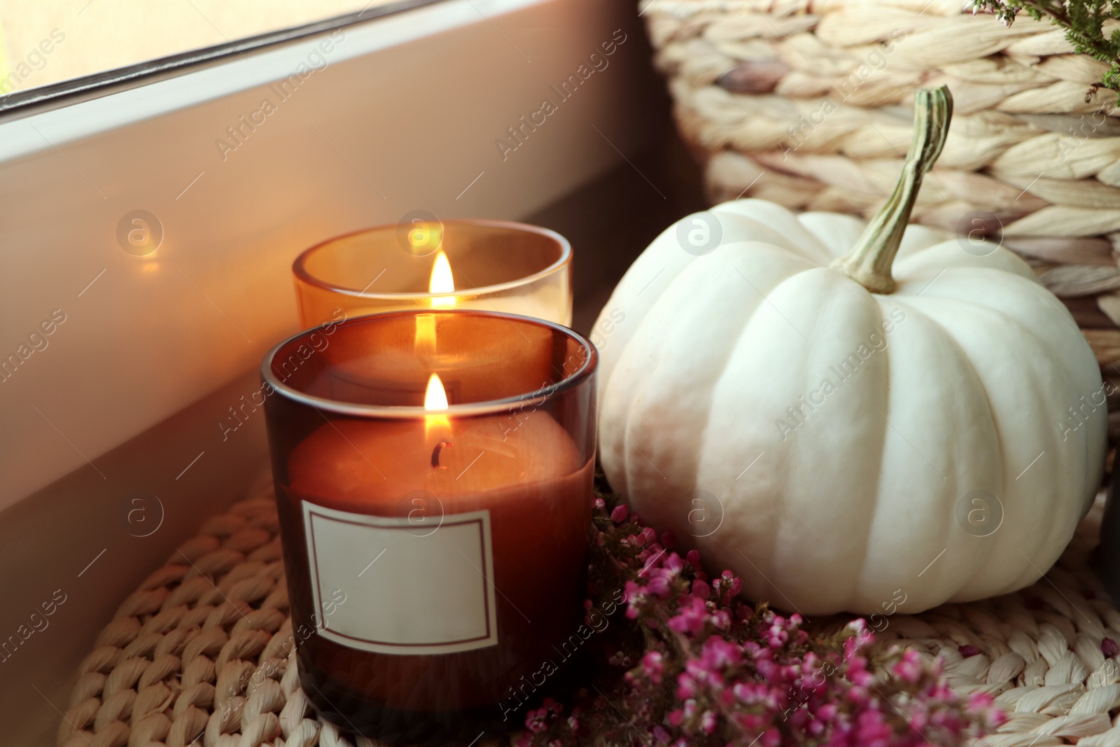 Photo of Beautiful heather flowers, burning candles and white pumpkin near window, closeup