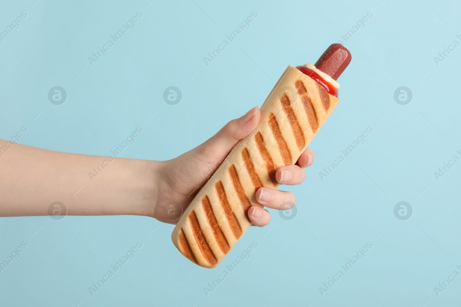 Photo of Woman holding delicious french hot dog on light blue background, closeup