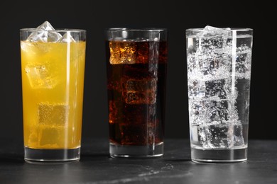 Glasses of different refreshing soda water with ice cubes on grey table