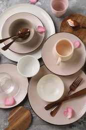 Stylish table setting. Dishes, cutlery, cup and petals on grey surface, flat lay