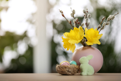 Photo of Festive composition with Easter eggs in decorative nest on table against blurred window, space for text