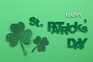 Happy St. Patrick's day card. Text and decorative clover leaves on green background, top view