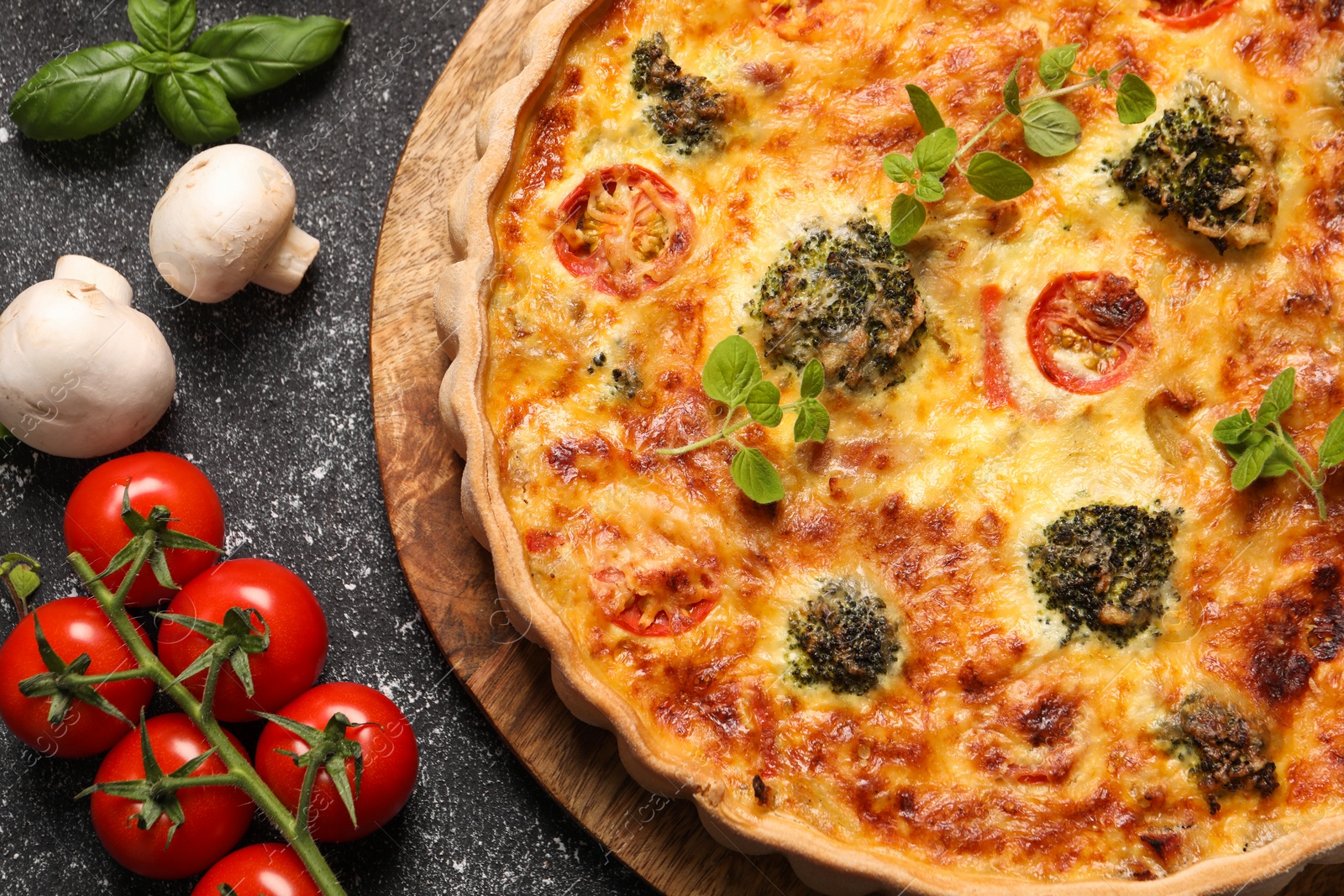 Photo of Delicious homemade vegetable quiche, oregano, tomatoes and mushrooms on black table, flat lay