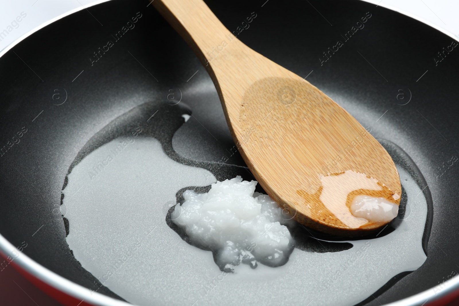 Photo of Frying pan with coconut oil and wooden spoon, closeup. Healthy cooking