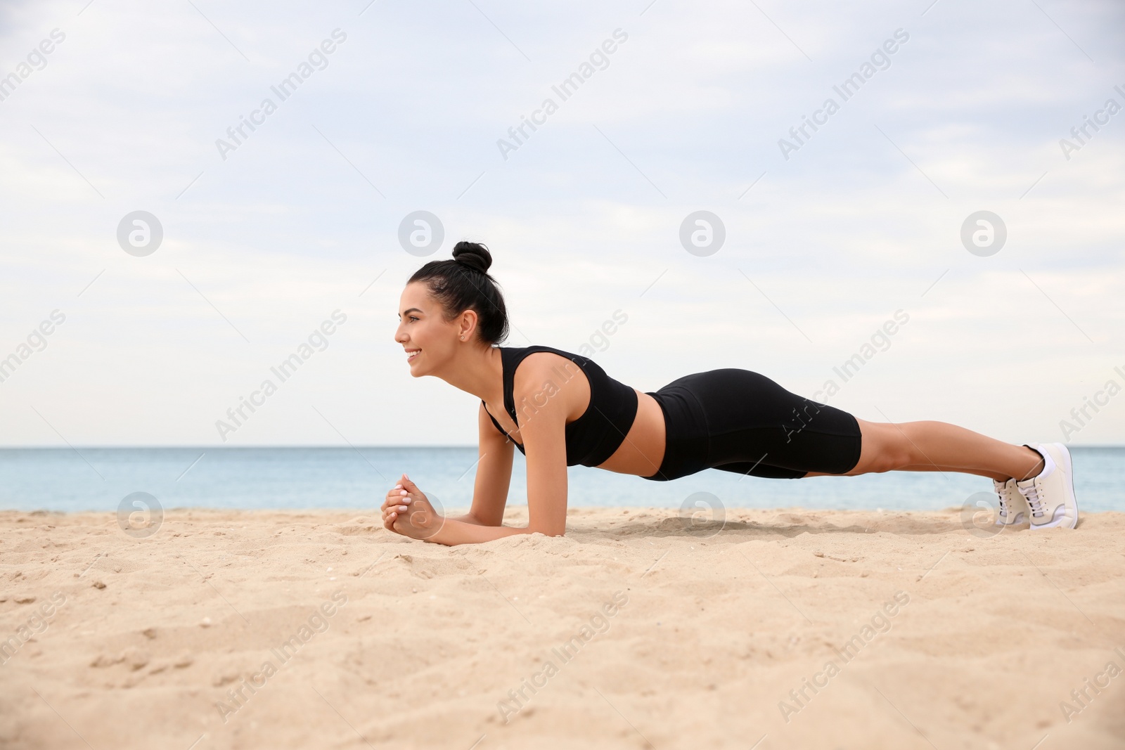 Photo of Young woman doing plank exercise on beach. Body training