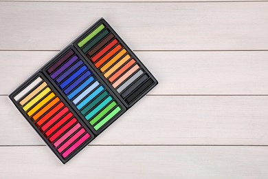 Photo of Set of colorful pastels in box on white wooden table, top view with space for text. Drawing materials