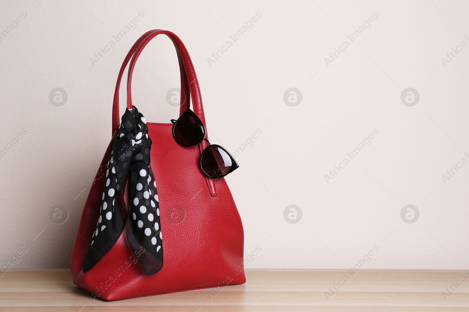Photo of Stylish red woman's bag, scarf and sunglasses on wooden table. Space for text