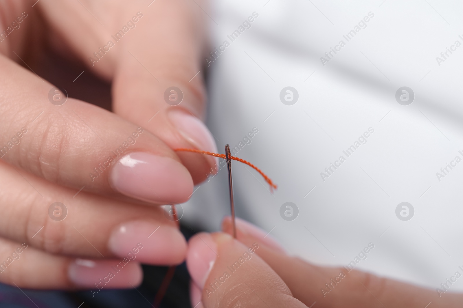 Photo of Woman inserting thread through eye of needle on blurred background, closeup