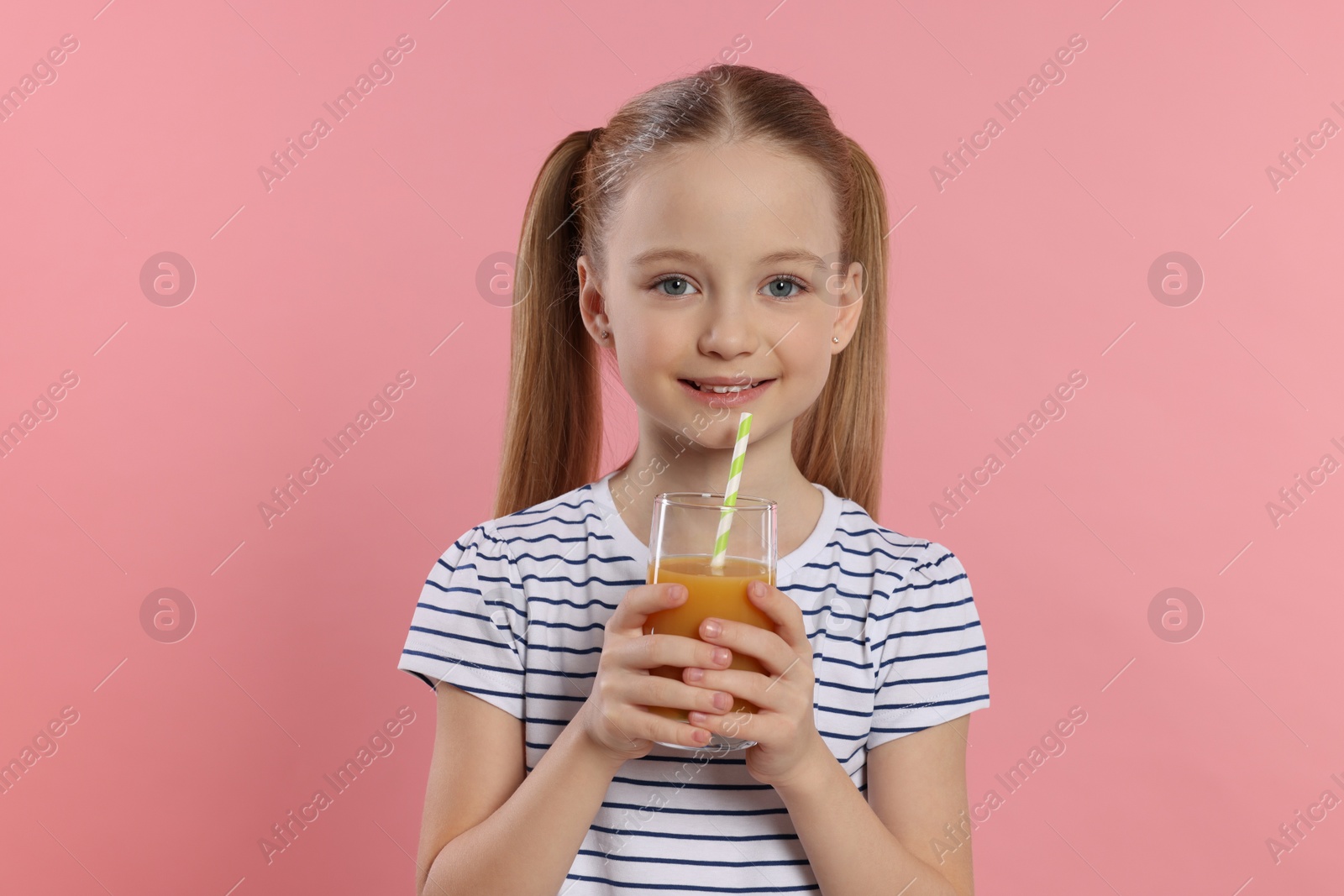 Photo of Cute little girl holding glass of fresh juice with straw on pink background