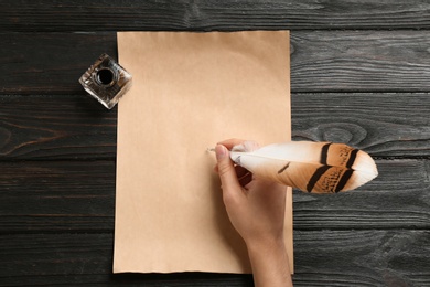 Woman using feather pen to write with ink on parchment at wooden table, top view. Space for text