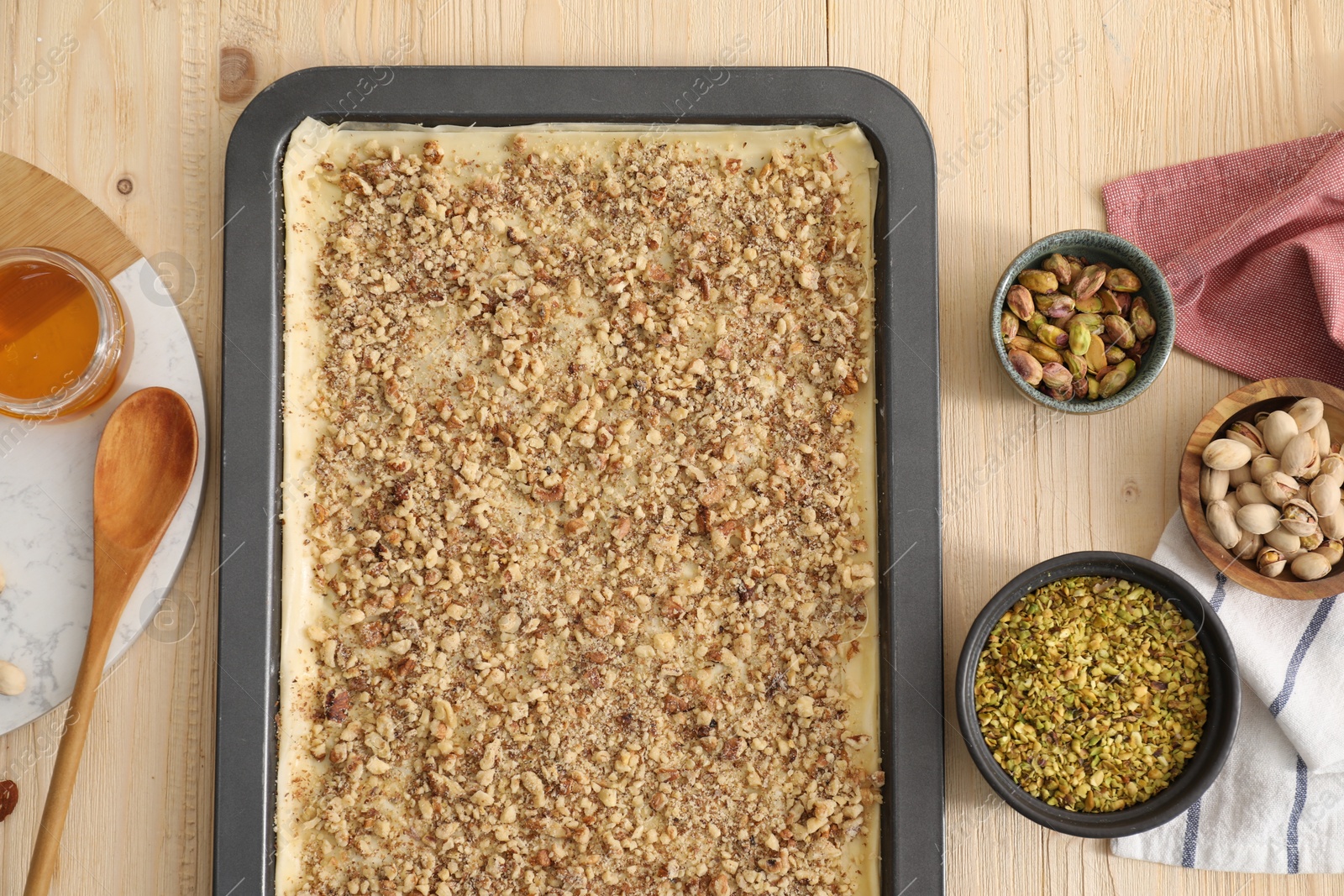 Photo of Making delicious baklava. Baking pan with dough and ingredients on wooden table, flat lay