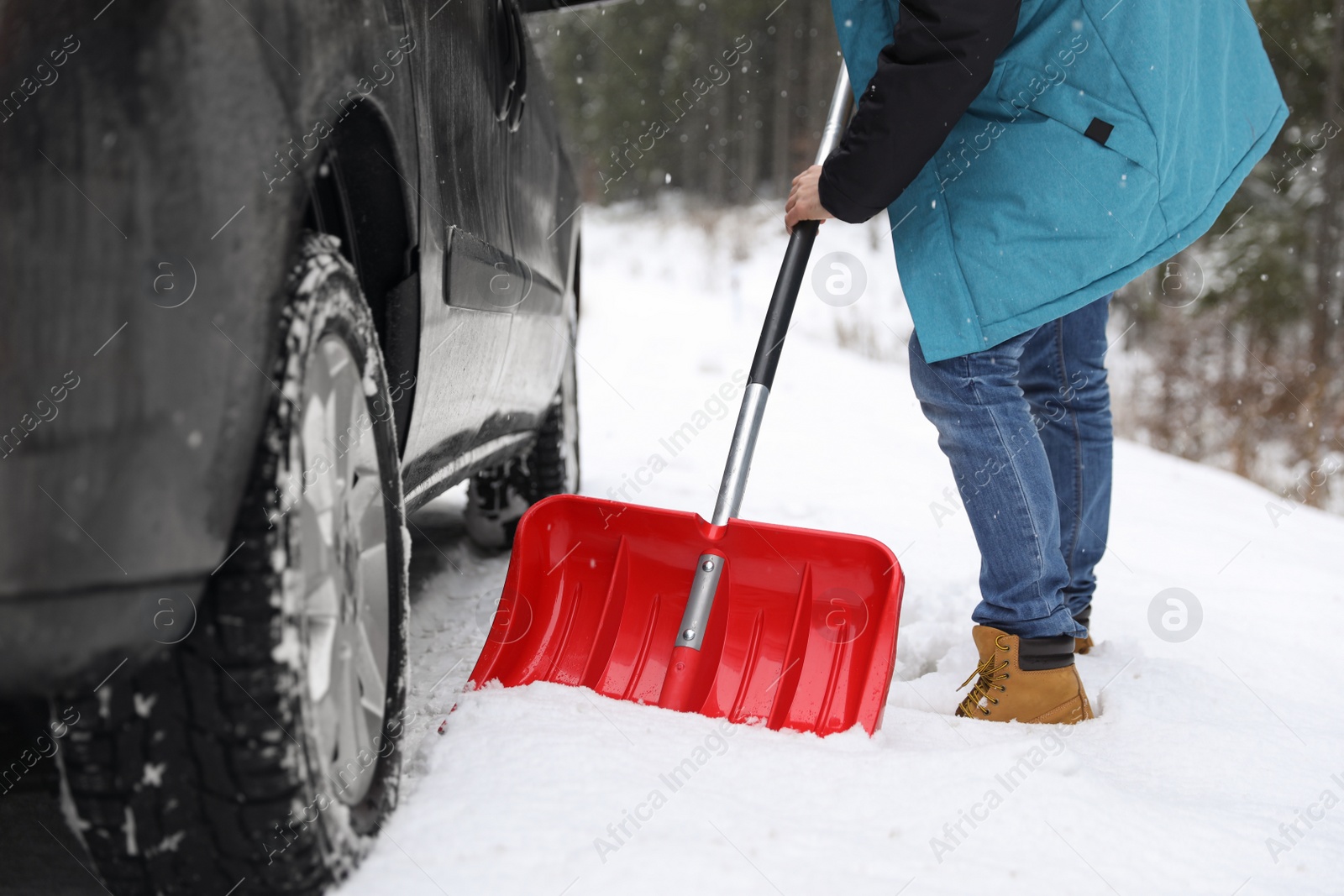 Photo of Man cleaning snow with shovel near stuck car outdoors