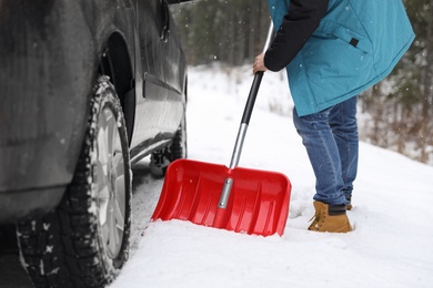 Photo of Man cleaning snow with shovel near stuck car outdoors