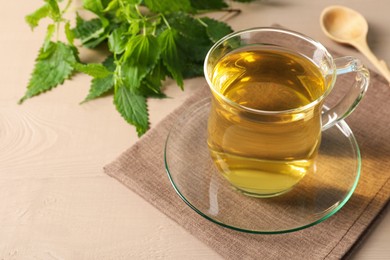 Glass cup of aromatic nettle tea and green leaves on wooden table, space for text