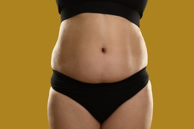Photo of Woman with excessive belly fat on goldenrod background, closeup. Overweight problem