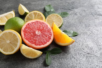 Photo of Different fresh citrus fruits and leaves on grey textured table, closeup. Space for text