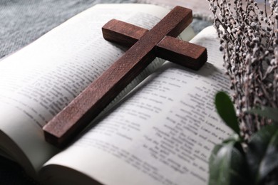 Photo of Bible, wooden cross and bouquet with willow branches on table, closeup