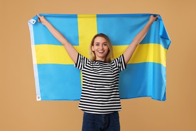 Happy woman with flag of Sweden on beige background