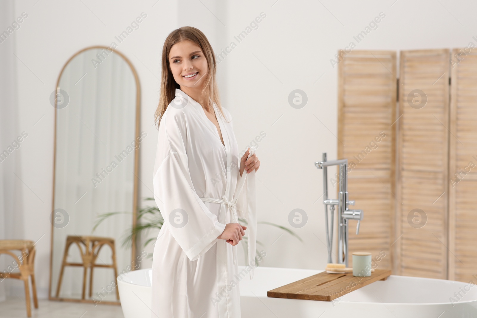 Photo of Beautiful happy woman wearing white robe near tub in bathroom. Space for text