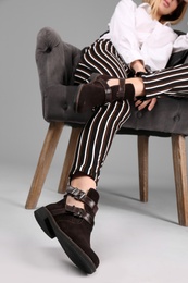 Photo of Young stylish woman with trendy shoes sitting in armchair on grey background